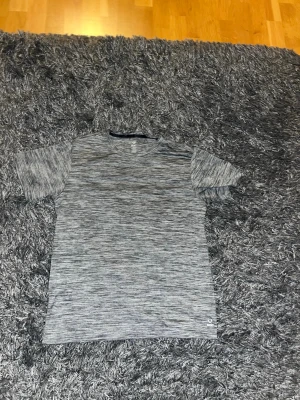 Träningströja från SOC - Säljer en gråmelerad t-shirt från SOC i storlek L. Tröjan är kortärmad och tillverkad i ett lätt och funktionellt syntetmaterial som andas, perfekt för träning. Diskret logga nere vid fållen och sportig look.