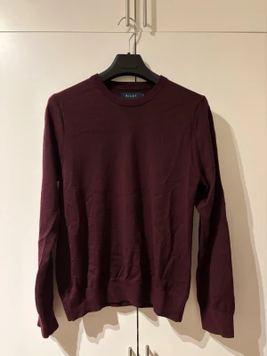 Vinröd merinoull-tröja från Riley – toppskick  - Säljer en stilren vinröd tröja i 100 % merinoull från Riley i toppskick. Den är väldigt mjuk och skön att bära, håller formen bra och funkar perfekt både till vardags med jeans och till lite finare tillfällen. Tröjan har en klassisk passform och en tidlös färg som är lätt att matcha. Den är knappt använd och i mycket fint skick.