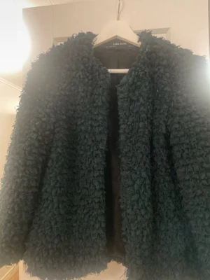 Mörkgrön teddyjacka från Zara Basic - Säljer en fluffig och mysig mörkgrön teddyjacka från Zara Basic i storlek XS. Jackan har långärmad design och en cool struktur med tätt lockigt material som ger en trendig look. 