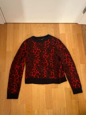 Röd leopardmönstrad stickad tröja LMTD - Säljer en stickad tröja från LMTD i rött och svart med leopardmönster. Tröjan har rund hals och lång ärm. Perfekt för dig som vill sticka ut med en cool och trendig look.