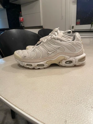 Nike vita sneakers Air Max Tuned - Nike Air Max Tuned sneakers i vitt med snygga vågiga detaljer på ovansidan och synlig Air-sula. Skorna har snörning och rund tå, och är tillverkade i syntetmaterial och mesh. Perfekt för dig som gillar klassiska och sportiga sneakers med chunky vibe.