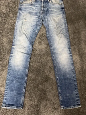 Blå straight jeans med slitningar - Snygga blå jeans med slitningar och tvättad look. Modellen har raka ben och klassisk femficksdesign. Jeansen har en ljusare tvätt framtill och är tillverkade i jeansmaterial, perfekta för en avslappnad stil.