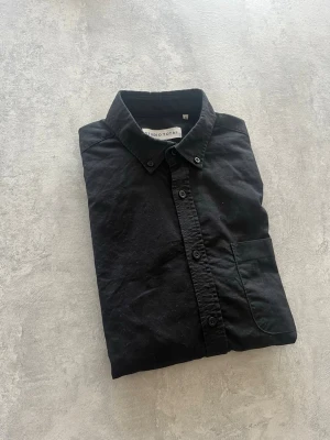 Studio Total Skjorta - Klassisk svart skjorta från Studio Total med knappar framtill och bröstficka. Skjortan har en stilren design med normal passform och är tillverkad i mjuk bomull. Perfekt att styla lager på lager eller bära som den är. Utmärkt skick. Storlek S.