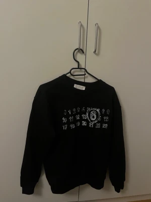 Maison Margiela sweatshirt - Cool svart sweatshirt från Maison Margiela med deras ikoniska siffror tryckta i vitt på bröstet. Tröjan har rund halsringning och ribbade muddar vid ärmslut och nederkant. Perfekt för dig som gillar minimalistisk och stilren design. Tröjan är självklart äkta och aldrig använd! Tveka inte att höra av er vid frågor eller funderingar🤗
