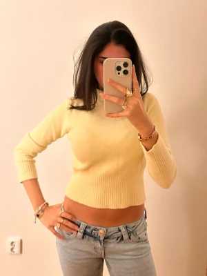 Gul croppad stickad tröja - Trendig ljusgul stickad tröja med croppad passform och långa ärmar. Tröjan har ribbstickade muddar vid ärmslut och midja, vilket ger en snygg siluett. Perfekt att styla med jeans för en avslappnad look.