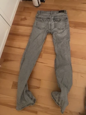 Grå bootcut jeans med kontrastsömmar - Säljer ett par gråa bootcut jeans med tydliga kontrastsömmar och klassiska fem fickor. Jeansen har en avslappnad passform och är tillverkade i ett mjukt denimtyg. Perfekta för dig som gillar en retroinspirerad look.