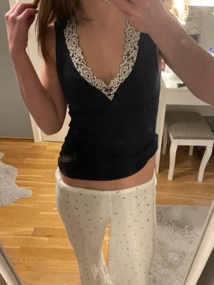 Marinblå linnetopp med spets från Intimissimi - Supersnygg svart linnetopp från Intimissimi med v-ringning och dekorativ vit spets längs ringningen. Toppen är ärmlös och har en tight passform som framhäver figuren. Perfekt att styla med jeans eller kjol för en trendig look. använda endast en gång!