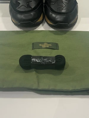 Valentino Garavani svarta sneakers - Säljer ett par svarta Valentino Garavani sneakers med stjärndetaljer på ovandelen. Skorna har rund tå, svarta snören och en kontrasterande brun detalj på sulan. Tillverkade i skinn och levereras med originalpåse och extra skosnören.