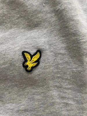 Grå sweatshirt från Lyle & Scott - Grå sweatshirt med rund hals från Lyle & Scott. Tröjan har det klassiska gula örnloggan broderad på bröstet och ribbade muddar vid ärmslut och nederkant. Perfekt för en avslappnad och stilren look.
