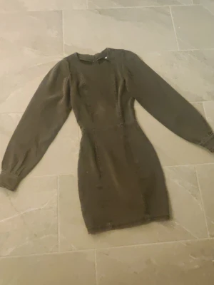 Mörkgrå jeansklänning Divided H&M - Supersnygg mörkgrå kort klänning i jeanstyg från Divided H&M. Klänningen har långa puffärmar och markerad midja som ger en riktigt trendig siluett. Perfekt för dig som vill sticka ut lite extra med en unik look. Aldrig använd och inga synliga fläckar. Finns i storlek 32. 