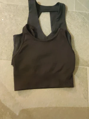 Svart sport-bh med brottarrygg - Säljer två olika svarta sport-bhar med brottarrygg och ribbad struktur. Dem har har bred resår nedtill för extra stöd och är tillverkad i ett stretchigt material som passar perfekt för träning eller chill. Dem båda är från Kappahl med märket Kayday, diskret broderat på nederkanten. Aldrig använda. 