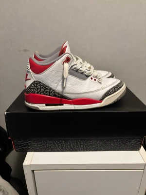 Nike Air Jordan 3 retro fire red - Air Jordan 3 Retro “White Fire Red Black” – Strl 40,5  Säljer ett par Nike Air Jordan 3 Retro i den klassiska färgkombinationen White / Fire Red / Black. En ikonisk modell med elefantmönster och synlig Air-enhet.  Detaljer: 	•	Modell: Air Jordan 3 Retro 	•	Färg: White / Fire Red / Black 	•	Storlek: EU 40,5 (US 7 / UK 6.5 / 25,5 cm) 	•	Originalkartong medföljer  Skick: 	•	Använda men i fullt brukbart skick 	•	Normala tecken på användning: veck på lädret, smuts/slitage på sulorna (se bilder) 	•	In