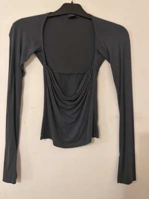 Mörkgrön långärmad topp från Gina Tricot -  mörkgrå långärmad topp från Gina Tricot med draperad front. Toppens material är mjukt och stretchigt, vilket ger en slim passform. Perfekt för dig som gillar en stilren men ändå unik look.