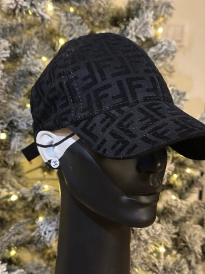 Svart keps med Fendi-logga - Snygg svart keps från Fendi med det klassiska FF-monogrammet över hela kepsen. Kepsen har böjd skärm och justerbar rem baktill. Perfekt accessoar för att lyfta din streetwear-look.