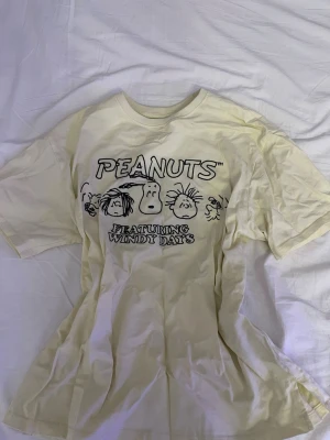 Gul Peanuts t-shirt från Zara - Cool gul t-shirt från Zara med Peanuts-tryck framtill och texten 'FEATURING WINDY DAYS'. Skön passform och klassisk rund hals. Perfekt för dig som gillar serietidningar och vill ha en avslappnad stil.