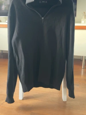 Svart stickad tröja med halvzip  - Svart stickad tröja med halv dragkedja och hög krage. Tröjan har lång ärm och ribbade muddar vid ärmslut och nederkant. 