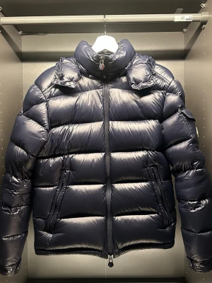 Moncler Maya - Säljer denna Moncler Maya i storlek 1 vilket motsvarar S, inköpt ny på NK i Stockholm vintern 2023 för 18 000 kr. Jackan är i mycket gott skick och sparsamt använd, säljs då den blivit för liten. Professionellt utförd lagning på ryggen (se bild). Färg: navy blue. Endast jackan ingår, kvitto och tags saknas. Pris kan diskuteras vid seriöst intresse. Hör av dig för fler bilder eller vid frågor och fundering. Mvh, Leo