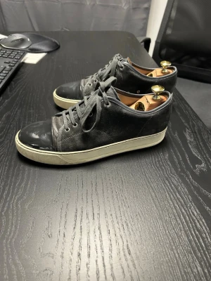 Lanvin sneakers herr – läder & mocka –grå – strl 40 - Snygga och exklusiva Lanvin sneakers för herr, i en stilren kombination av läder och mocka med kontrasterande gummisula. En tidlös premium-sneaker som passar både till vardag och mer uppklädda outfits.  Skorna är märkta storlek 40, men Lanvin är små i storleken – de passar snarare dig som normalt bär EU 41. Använda med normalt slitage, främst på sulorna (se bilder). Ovandelen i gott skick utan större skador.  Skoblock syns på bilderna men ingår ej.