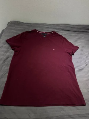 Vinröd t-shirt från Tommy Hilfiger - Snygg vinröd t-shirt från Tommy Hilfiger i extra slim fit. Tillverkad i mjuk bomull och har en liten diskret logga på bröstet. Klassisk rund halsringning och korta ärmar. Perfekt för en clean och stilren look. Passar även folk med storlek L då den är slim 