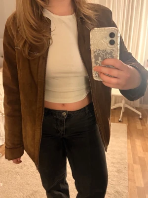 Brun mocka jacka från Livelo - Detta är en snygg brun jacka av vad jag tror är mocka från Livelo Attitude (baserat på lappen inuti). Jackan har dragkedja framtill, två bröstfickor med dragkedja och en klassisk rak passform. Perfekt för dig som vill ha en tidlös och cool vintage look. Jackan är mer åt oversized hållet om man är något kortare och mindre i storlek, men passar till alla och till allt🌟Den är använd men det är väl det som gör hela vintage looken😋Säljer för att den inte kommer till användning. Skriv för mer bilder! 