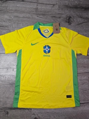 Brazil fotbollströja - Säljer en officiell Brasilien fotbollströja från Nike i klar gul färg med gröna och blå detaljer. Tröjan har CBF-emblem på bröstet och Nike-logga i grönt. Kragen är grön och materialet är lätt polyester, perfekt för fotboll och sport.