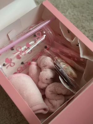 Rosa Gift Set - Säljer ett set med fluffiga rosa scrunchies och andra håraccessoarer i en söt presentförpackning. Scrunchiesen är gjorda i mjukt tyg och passar perfekt för att skapa en gullig look. Flera av accessoarerna har blommönster och rosa detaljer.