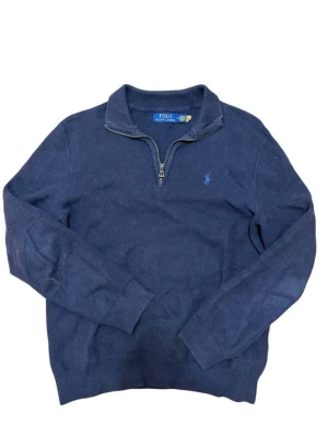 Marinblå halvzip från Polo Ralph Lauren - Klassisk marinblå tröja från Polo Ralph Lauren med halvzip och ståkrage. Tröjan har lång ärm. Och den ikoniska broderade loggan på bröstet. Perfekt för en stilren och avslappnad look.