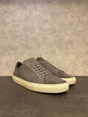 Axel Arigato Clean 90 - Stilrena Axel Arigato Clean 90s sneakers i mocka med vit platt sula och snörning. Skorna har en enkel och clean design med rund tå och diskreta sömmar. Perfekta för dig som gillar en minimalistisk look.I bra skick men finns vanligt slitage från användning men som inte påverkar helhetsintrycket!