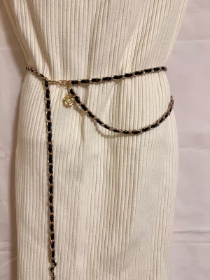 Kedjebälte med svarta detaljer och rosor - Säljer ett snyggt kedjebälte i guld med svarta inslag och två hängande rosberlocker. Bältet är 100 cm långt och passar perfekt att styla över klänning eller byxor för en trendig look.