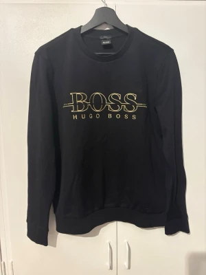 Svart Hugo Boss sweatshirt slim fit - Svart sweatshirt från Hugo Boss med logga på bröstet. Tröjan har rund halsringning, lång ärm och är i slim fit-modell. Tillverkad i mjuk bomull för skön känsla och stilren look.