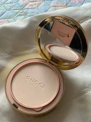 Gucci puderfoundation i en dosa - Puderfoundation i en elegant rund guldfärgad dosa med spegel. Pudret är ljust beige. Kommer med en mjuk applikator och ett separat fack för puffen. 