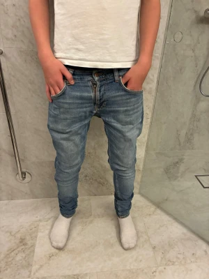 Ljusblå skinny jeans från Nudie - Snygga ljusblå  jeans från Nudie med klassiska bakfickor och broderad detalj. Jeansen har normal passform i midjan och är storlek 29x30 Hör av er vid frågor! Obs pris kan diskuteras!