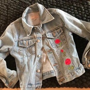 Jeansjacka - Säljer en snygg ljusblå jeansjacka från märket ”EXIT”. Har broderade blommor för en unik och snygg look. Storlek 10 år/140 cm men passar xxs och pris kan diskuteras