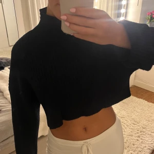 Mörkblå croppad stickad tröja - Säljer en mörkblå croppad stickad tröja med ribbad struktur. Tröjan har lång ärm och hög hals, perfekt för dig som gillar en trendig och avslappnad stil. Passformen är loose och den är superenkel att matcha med både jeans och kjol.