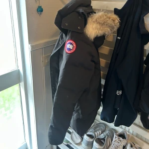 Svart dunjacka från Canada Goose - Hej! Säljer en svart jacka  från Canada Goose wyndham. Jackan har ett fint skick, samt en riktigt varm och puffig känsla. Perfekt för kalla vinterdagar och snygg till streetwear-stilen. Jackan är autentisk, storlek M 