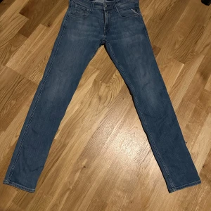 Replay Anbass blå jeans slim fit - Snygga blå Replay Anbass jeans med klassisk femficksdesign och diskreta slitningar. Jeansen har slim fit-passform, raka ben och detaljerade sömmar på bakfickorna. Perfekta till sneakers och hoodie för en chill look. Liten slitning i bakfickan men inget som märks. W29 L32