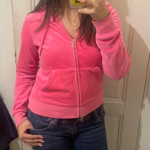 Juicy Couture rosa velour hoodie - Säljer en ikonisk rosa hoodie från Juicy Couture i mjuk velour. Tröjan har dragkedja framtill, huva och broderad logga på bröstet. 