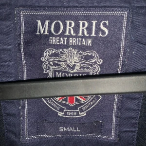 Svart sweatshirt från Morris med tryck - Säljer en svart sweatshirt från Morris i storlek small. Tröjan har broderad Morris-text och brittisk flagga på bröstet. Klassisk rund halsringning och ribbade muddar. Perfekt för dig som gillar stilren och sportig look. Hör av er vid minsta lilla 