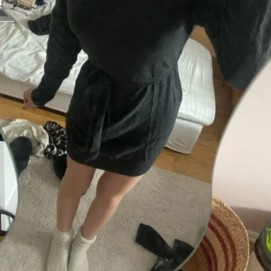 Mörkgrå stickad klänning H&M S - Mysig mörkgrå stickad klänning från H&M i storlek S. Modellen är kort med långa ärmar och har ett matchande bälte i midjan för snygg passform. Perfekt för dig som gillar enkel och stilren look med lite extra cozy-vibe.