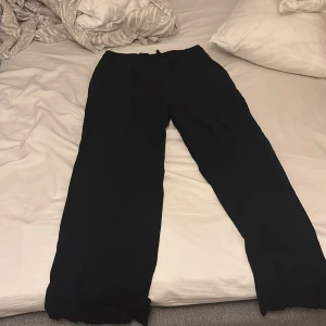 Svarta vida byxor från 157, XS - Svarta byxor från 157 i storlek XS. De har en avslappnad, vid passform och resår i midjan med snörning för extra komfort. Perfekta för en chill och stilren look. Materialet känns mjukt och lätt, vilket gör dem sköna att bära hela dagen. Gjorda för 160 cm ner åt korta vid benen för folk som är över 160 cm 