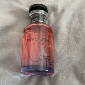 Louis Vuitton City of Stars parfym 100ml - Exklusiv parfym från Louis Vuitton, City of Stars, i en snygg glasflaska med rosa och lila toner. Flaskan rymmer 100 ml Eau de Parfum och har en elegant svart och silverfärgad kork. Perfekt för dig som gillar lyxiga dofter och stilren design.
