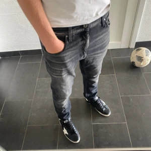 Tiger Of Sweden Jeans - Snygga svarta jeans från Tiger of Sweden i modellen Pistolero. Jeansen har en tvättad look med ljusa slitningar och klassisk femficksdesign. Passformen är rak med något smalare ben. Perfekta till sneakers och t-shirt för en avslappnad stil.