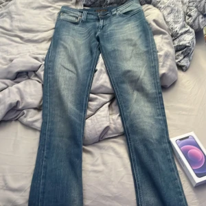Blå jeans från Nudie Jeans Co - Säljer ett par klassiska blå jeans från Nudie Jeans Co i modellen W27 L32. Jeansen har en snygg tvätt med slitningar och raka ben. Tillverkade i 100% ekologisk bomull och har Nudie-loggan på bakfickan. Perfekta för dig som gillar en tidlös denimlook. Diskutera pris 