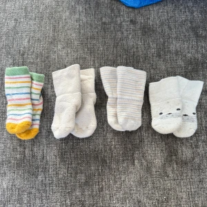 Fyra par mjuka barnstrumpor - Säljer fyra par gulliga barnstrumpor. Ett par är randiga i grönt, gult, rosa, blått och vitt. Ett par är helvita och fluffiga. Ett par har tunna grå och beige ränder. Ett par är vita med sött djuransikte framtill. Alla är i mjukt bomullsmaterial och har normal passform.