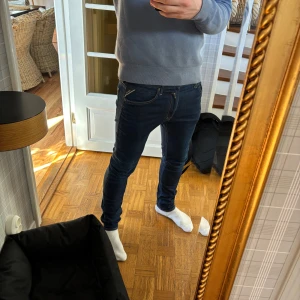 Mörkblå skinny jeans med snygga detaljer - Säljer ett par mörkblå slim fit jeans från Replay med klassiska femficksdetaljer och snygga kontrastsömmar på bakfickorna. Jeansen har låg midja och är tillverkade i stretchig denim för en tight passform. Perfekta för dig som gillar en modern och stilren look.