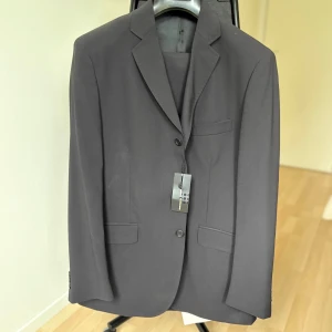 Svart kostym – Mediterranea, Made in Italy (stl 52) - Helt ny svart kostym från italienska Mediterranea. Elegant och klassisk modell med två knappar, svart sidenfoder och matchande byxor med pressveck. Perfekt både till fest och business.  Storlek: 52  Färg: Svart (col. 12)  Märke: Mediterranea – Made in Italy  Nypris: 4495 kr  Skick: Ny med tags