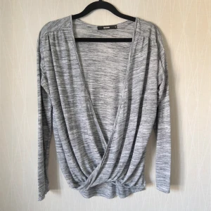 Grå omlottopp från Bik Bok - Snygg gråmelerad omlottopp från Bik Bok med lång ärm och djup v-ringning. Tunt material och skönt material. Bredd 52 cm, Längd 52 cm