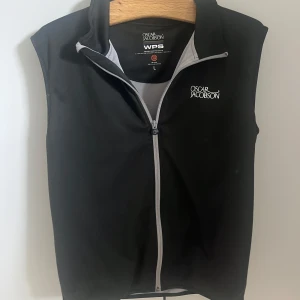 Svart väst från Oscar Jacobson - Svart väst från Oscar Jacobson med vit logga på bröstet och ryggen. Västen är L men sitter som M