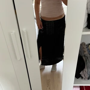 Svart långkjol med slits  - Svart långkjol från AMSU med snygg slits på sidan som ger en cool vibe. Kjolen är rak i modellen och gjord i mjukt bomullstyg, vilket gör den skön att bära. 