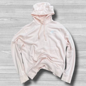 Ljusrosa hoodie från Nike - Säljer en ljusrosa hoodie från Nike med broderad logga på bröstet. Tröjan har huva med snörning, känguruficka och är tillverkad i mjuk bomullsmix. Perfekt för en chill och sportig look.